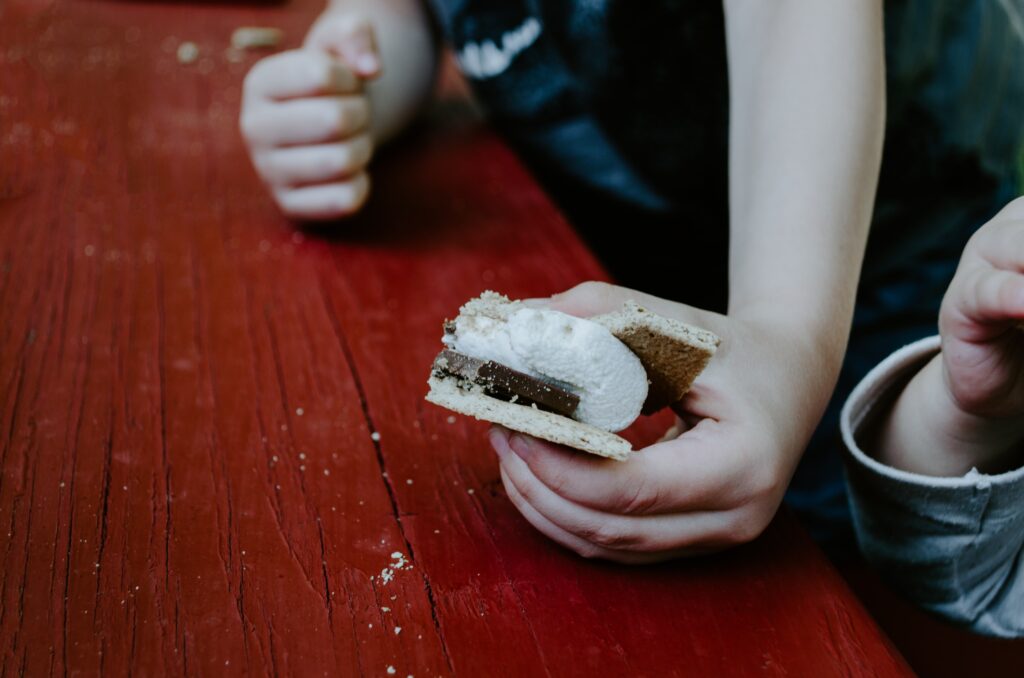 Child holding a s'more on a picnic table.