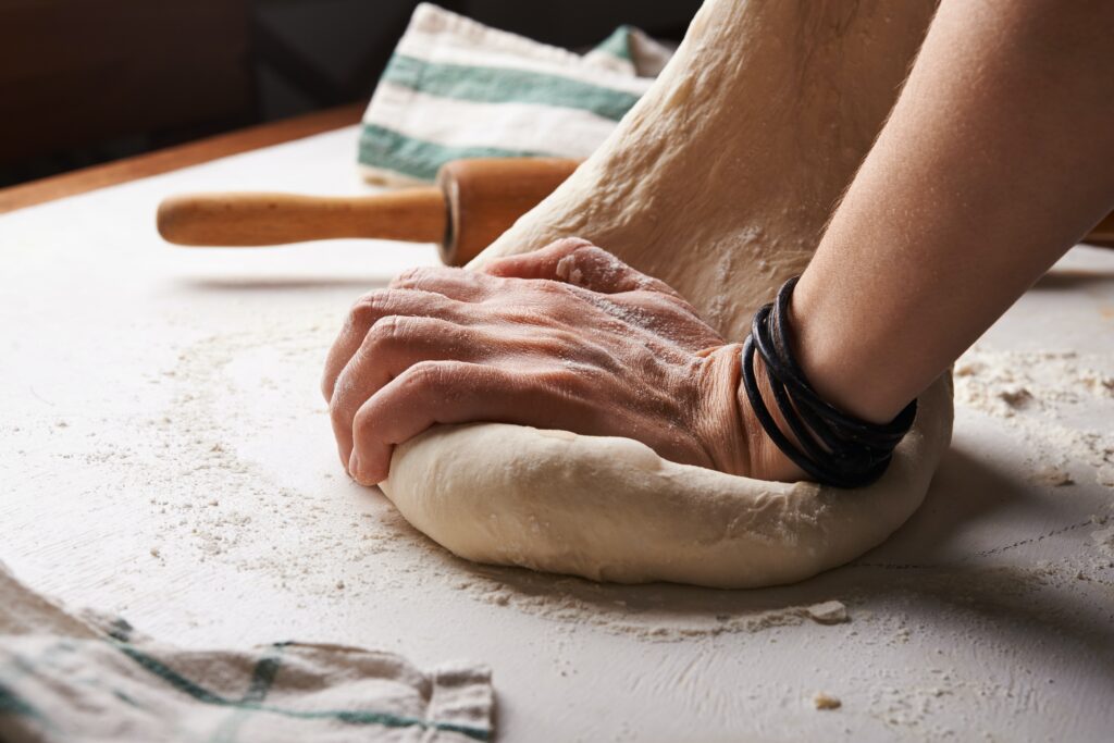 person kneading dough with flour around the dough and a rolling pin.
