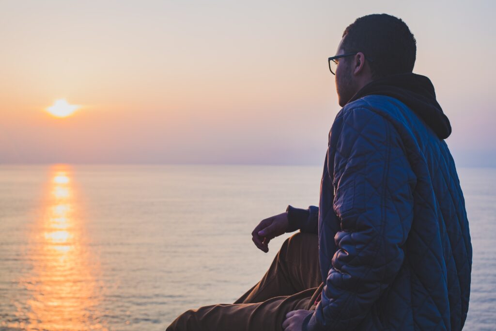 man staring at the morning sunrise and looking out over a large body of water. 